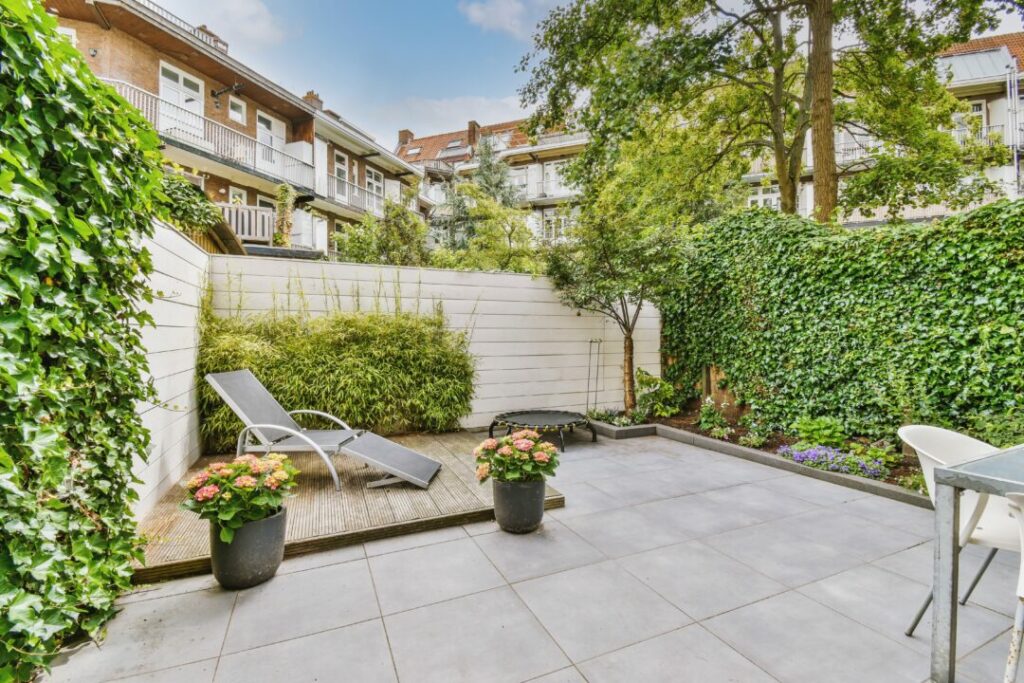 Modern courtyard garden with a sleek tiled patio, lush ivy-covered walls, and a wooden decked lounging area. A stylish and minimalist example of courtyard garden ideas for small urban spaces.