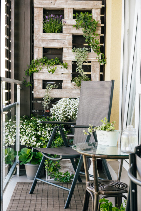 Small balcony with wooden vertical planters, lush greenery, and a cosy seating area – a space-saving small balcony idea.
