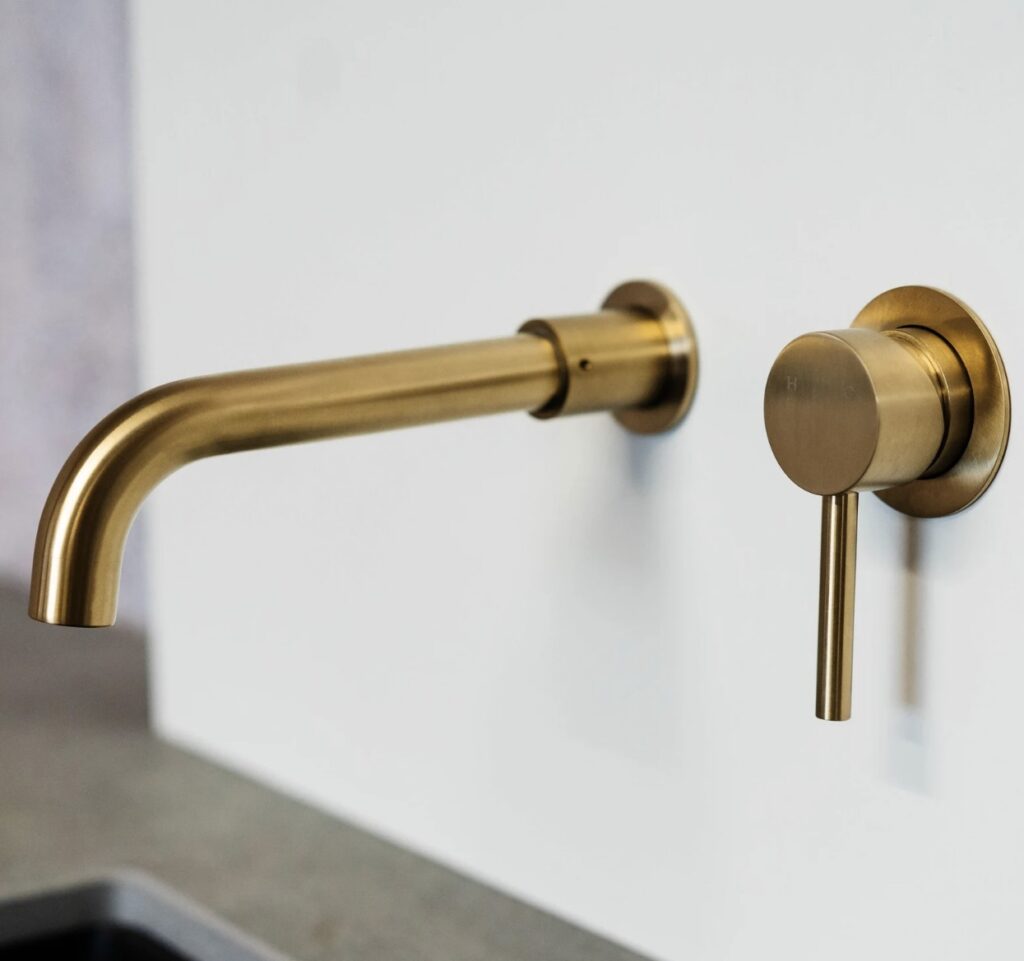 Gold wall-mounted bathroom tap fitting above coloured basin.