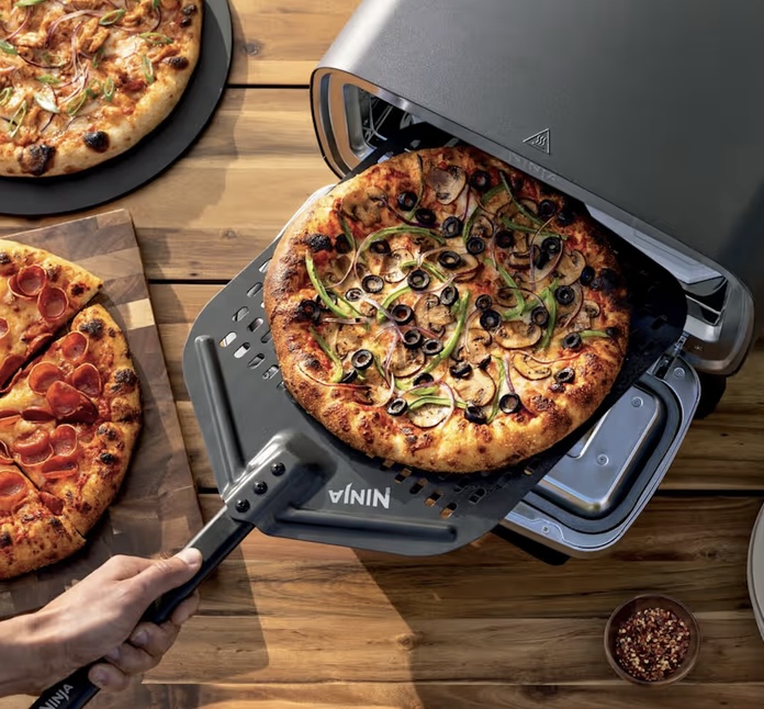 Ninja Artisan electric outdoor pizza oven with a freshly baked pizza on a paddle, set for alfresco dining.
