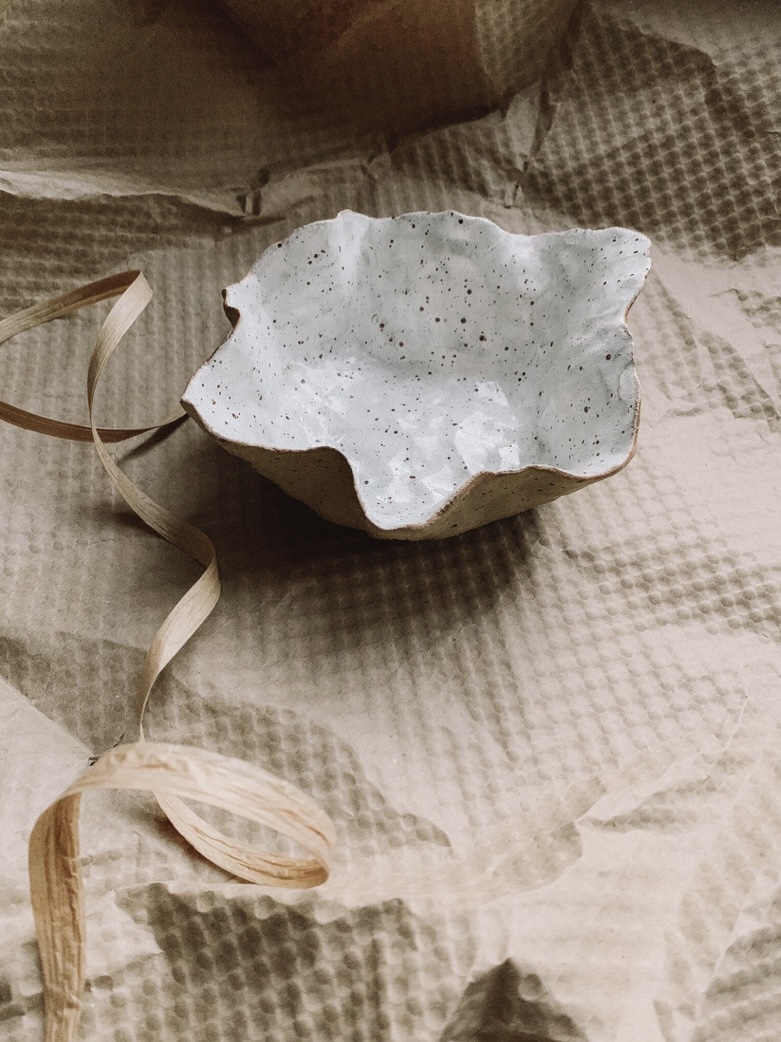 Handmade ceramic petal bowl with white flecked glaze; organic accent on a black console table