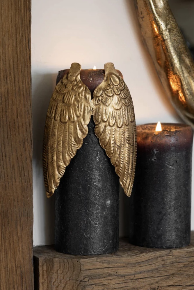 Gold winged metal candle decoration clipped to a taper candle on a console