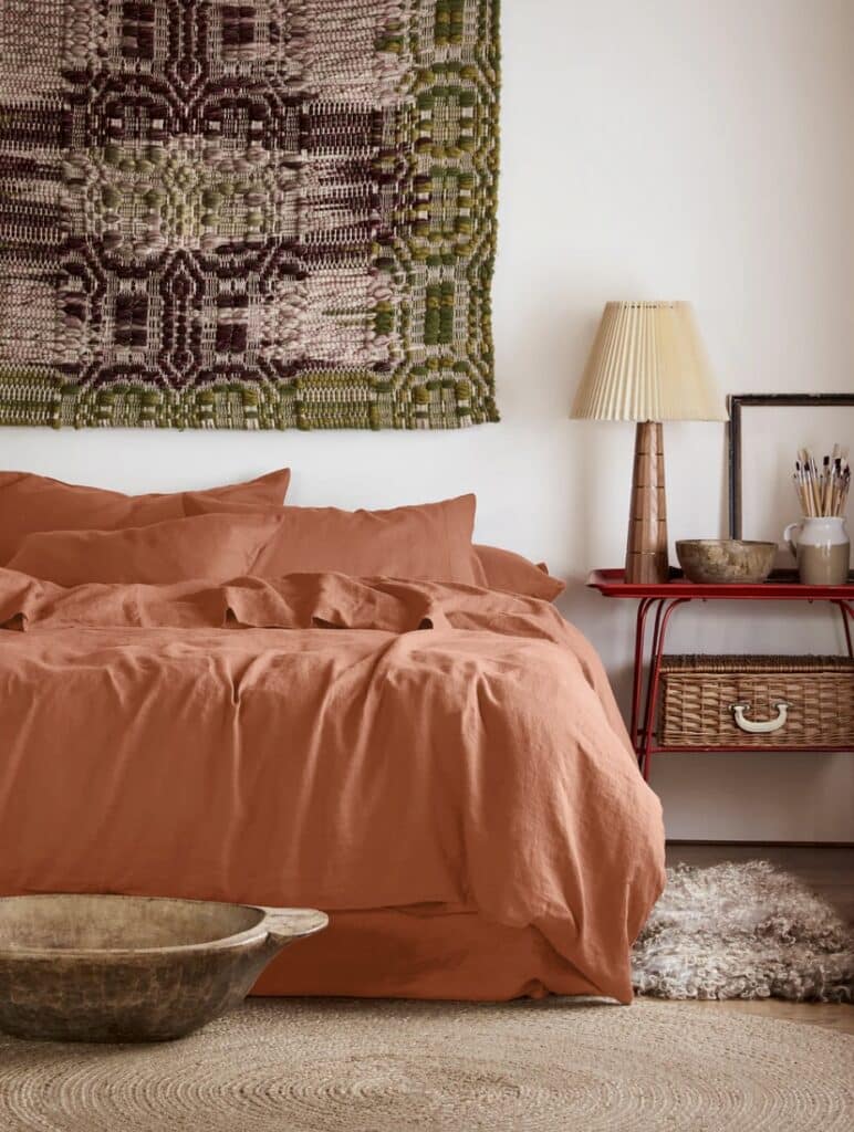 Burnt orange bedding layered on a relaxed bed with boho textures (woven wall hanging, jute rug and basket) for cosy boho bedroom ideas.
