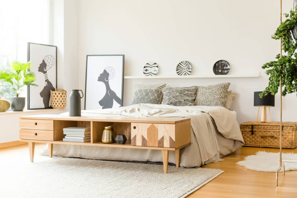 Boho bedroom storage idea with a low wooden cupboard at the end of the bed, neutral bedding and simple wall art