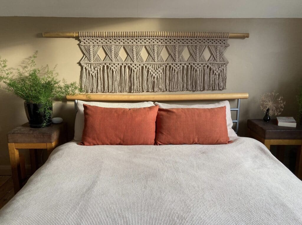 Boho chic bedroom ideas with a large neutral macramé wall hanging above the bed and warm terracotta cushions.