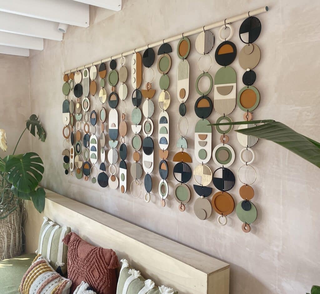 Statement wall hanging above a bed in a boho bedroom, with colourful geometric discs and layered cushions.