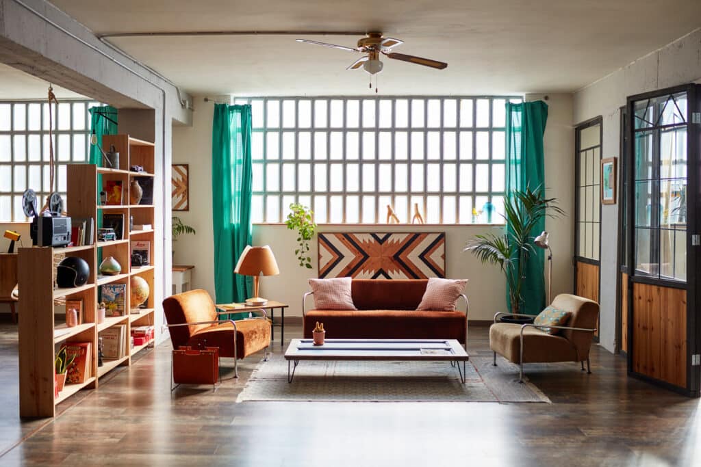 Eclectic living room with rust velvet sofa, teal curtains, open shelving and geometric wall art panel
