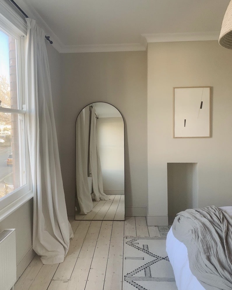 Feng shui mirror, an arched full-length mirror reflecting natural light in a calm bedroom