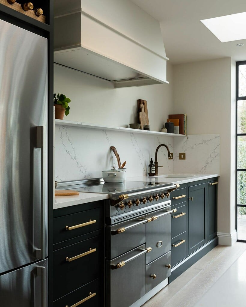 Galley kitchen with base units painted in Studio Green, a range cooker, a marble splashback and a long floating shelf beneath a plastered extractor hood