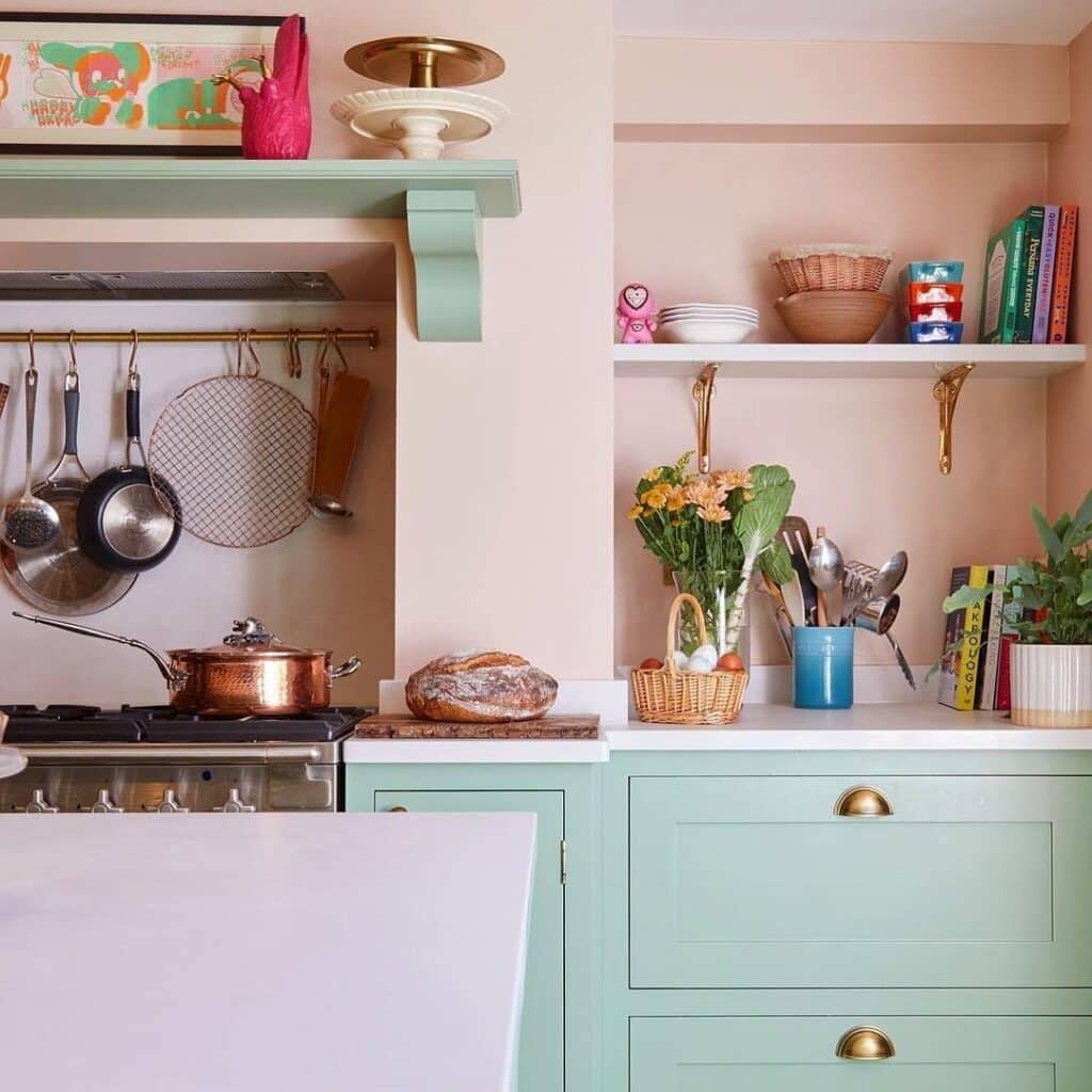 Two tone kitchen with Farrow & Ball Breakfast Room Green lower cabinets, Setting Plaster pink walls, brass cup handles, open shelving and a traditional range cooker.​​​​​​​​​​​​​​​​