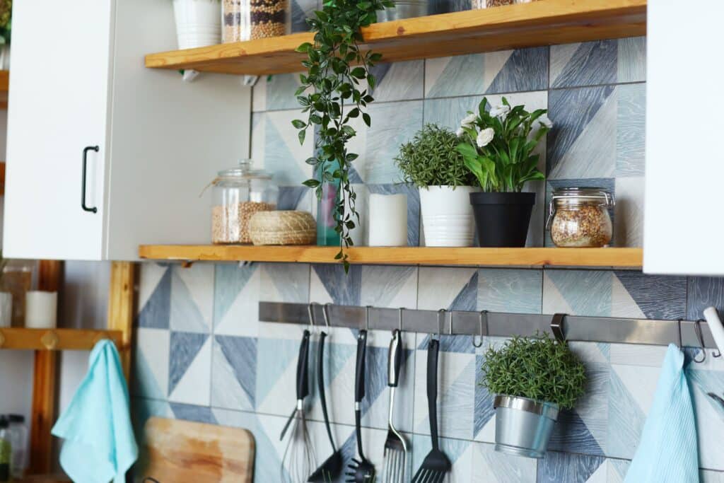 Rustic kitchen floating shelves with plants, glass jars, and utensils against a geometric tile backsplash.