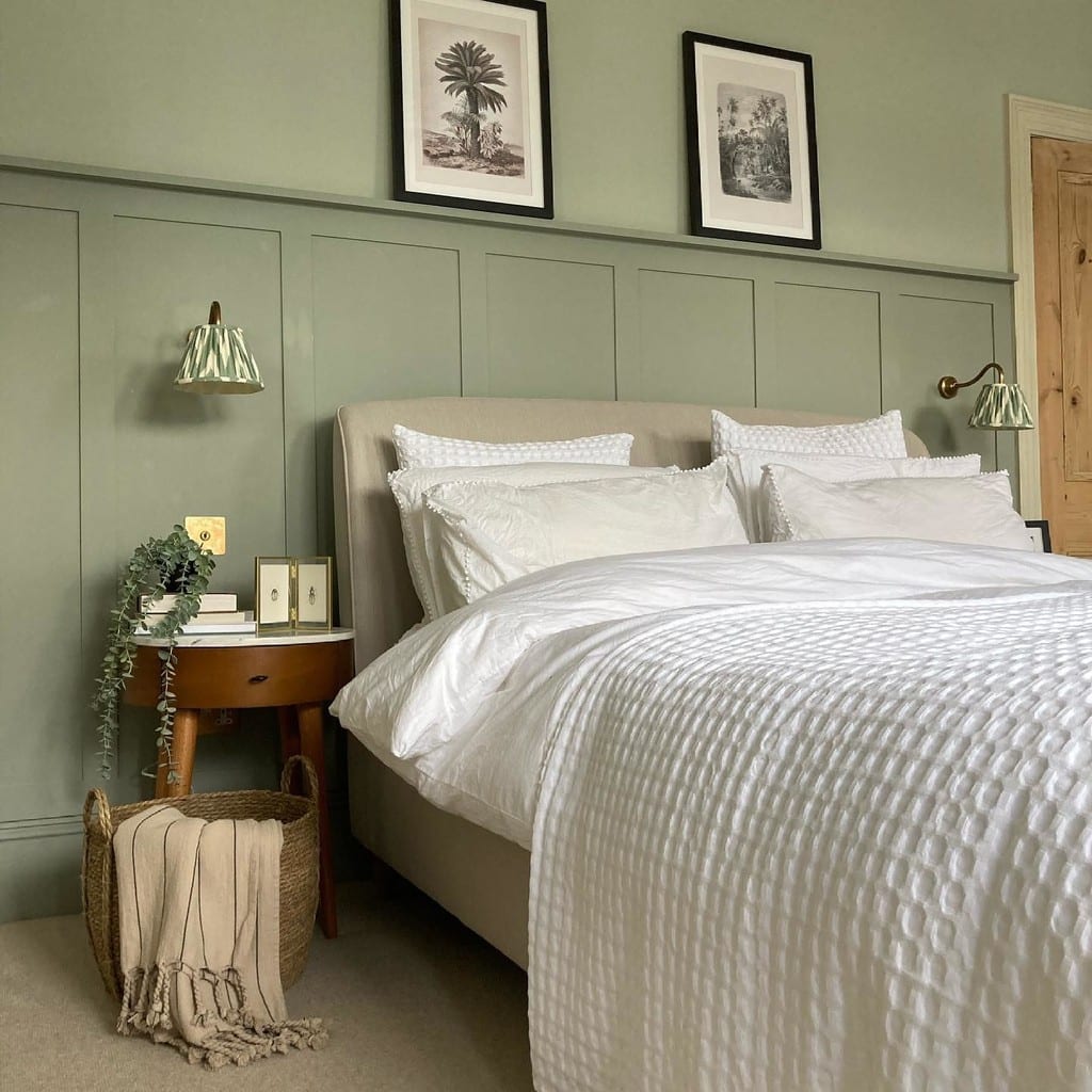 Pair of engraved palm tree prints in black frames above a bed with sage green panelling
