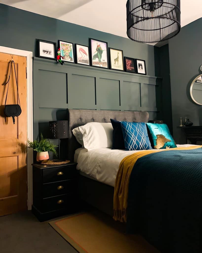 Eclectic framed prints leaning on a panelling ledge above a bed in a dark Down Pipe bedroom