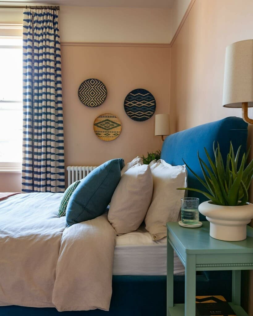Three round woven basket plates hung in a cluster on a pink bedroom wall beside a blue headboard