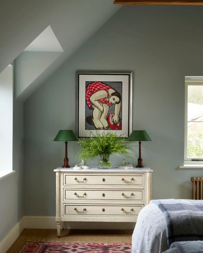 Bold figurative print in a silver frame above a cream chest of drawers between two green lamps in a Light Blue bedroom