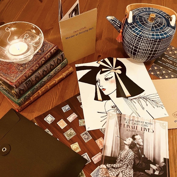Murder mystery game props including vintage postcards, candle and notebook