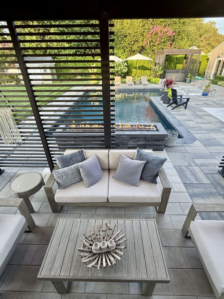 Pergola-covered patio with outdoor sofa and linear fire feature beside a pool