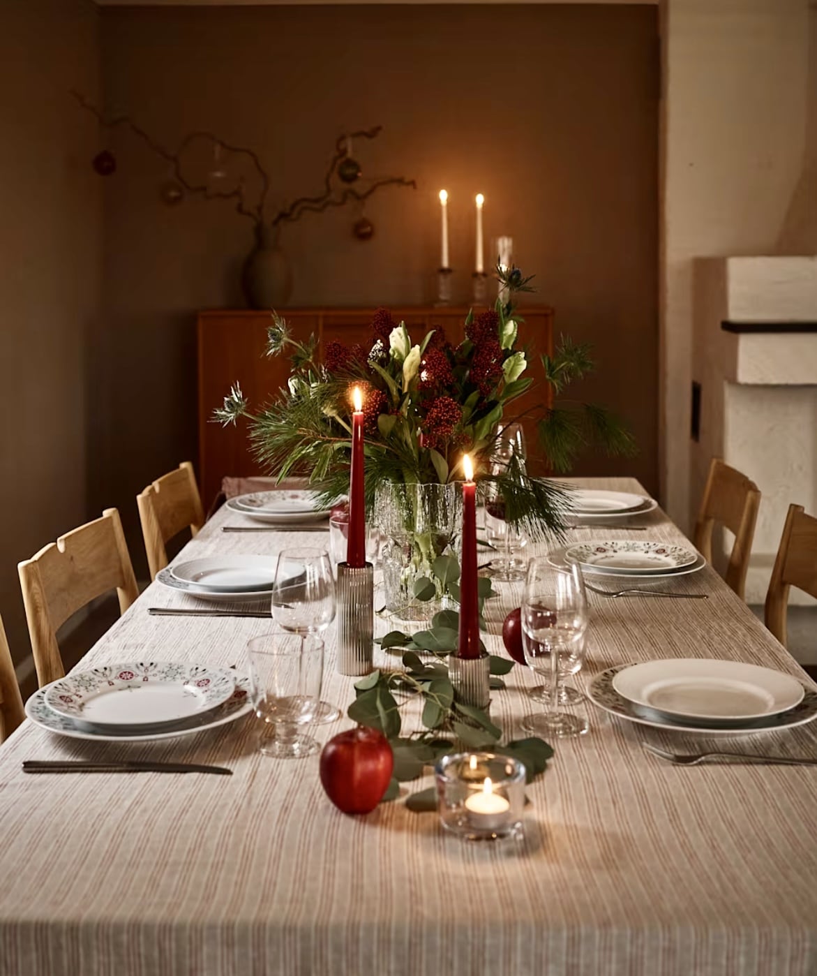 Candlelit Christmas table setting with greenery, red accents and simple white plates – cosy Christmas table setting ideas for guests