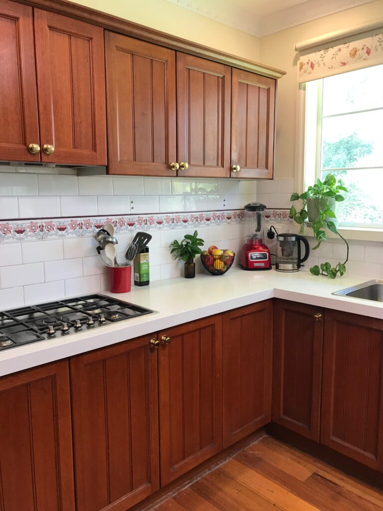 Kitchen before renovation with dark timber Shaker-style cabinets, brass knobs, a floral border tile splashback and white quartz worktops