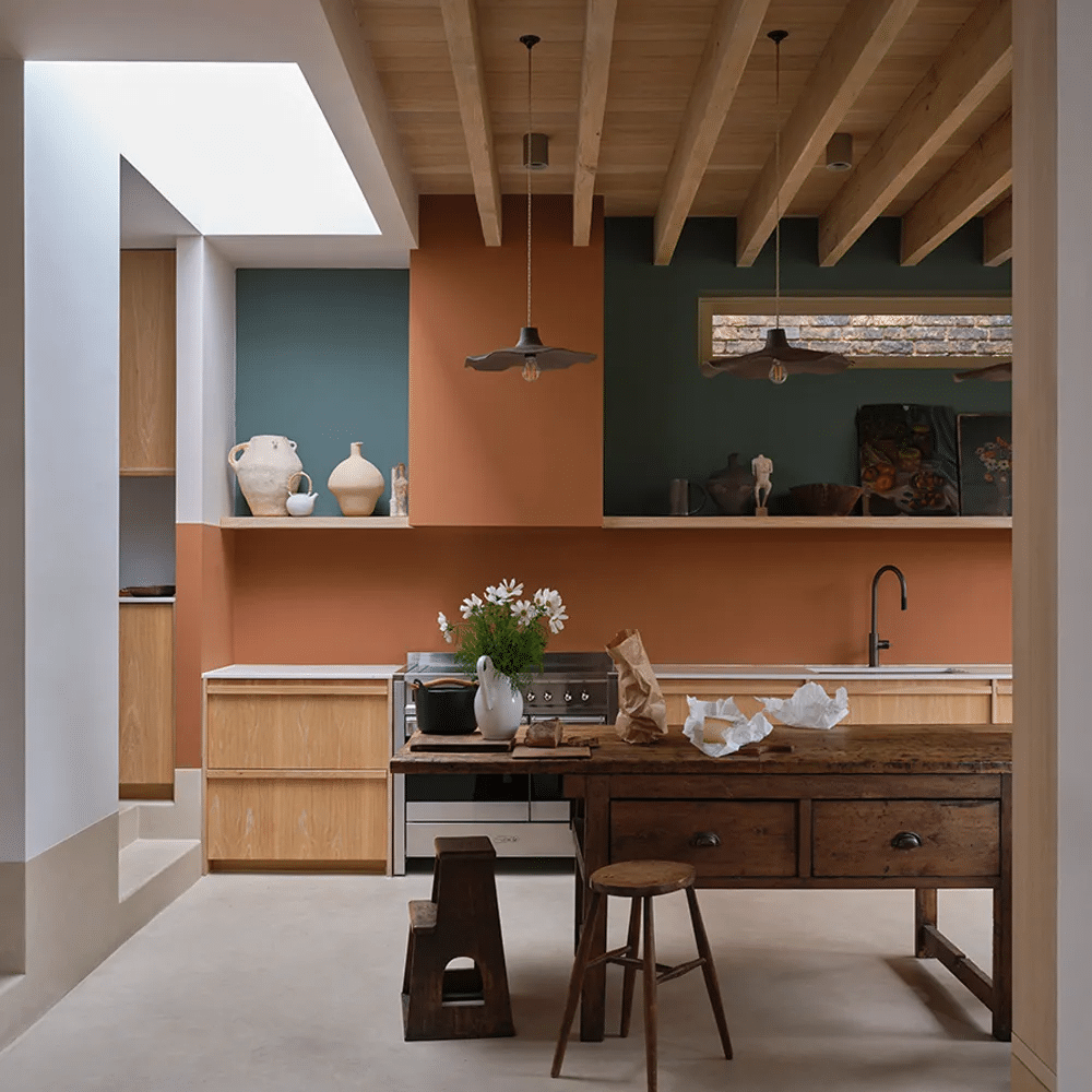 Kitchen with walls in Marmelo terracotta and deep green, oak units, an antique wooden workbench used as an island and exposed timber ceiling beams