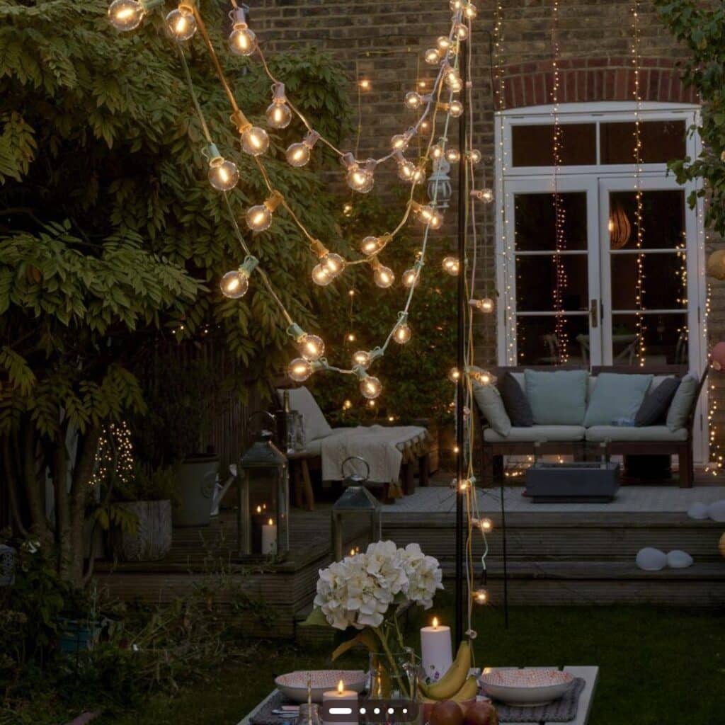 layered outdoor party lighting with festoon lights fairy lights and candles in a garden seating area