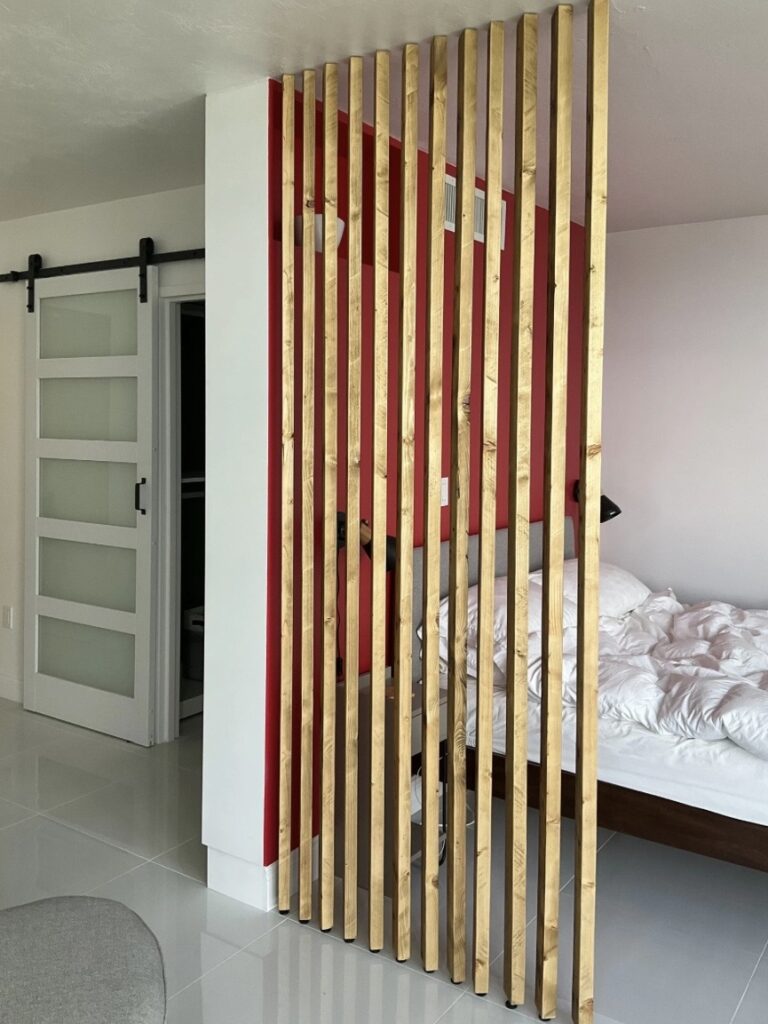 Bedroom room divider ideas: RobertRoseCarpentry Georgina wooden wall partition creating a sleeping zone with red accent wall and sliding barn door