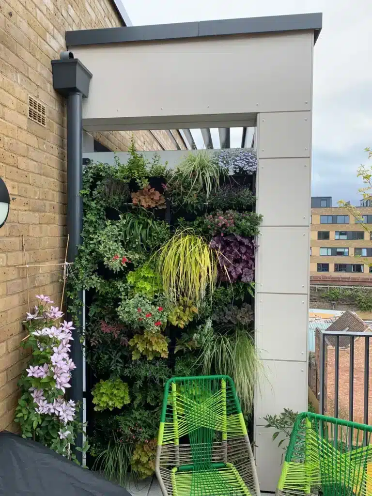 Modular outdoor living wall with flowering clematis beside a contemporary pergola and lime green garden chairs