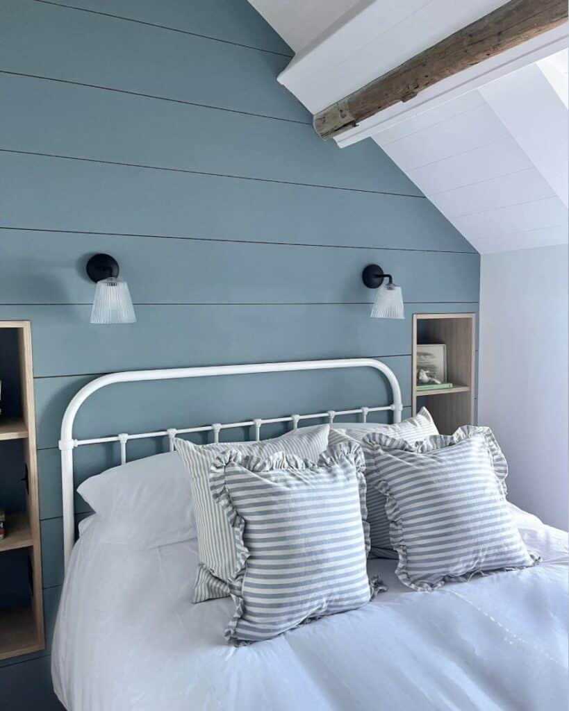 Shiplap-panelled sloped ceiling bedroom in soft sea-blue with an iron bedstead.