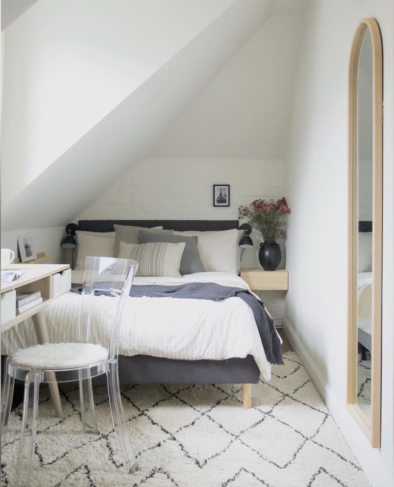 Bed tucked under a sloped ceiling with a full-length mirror in a small bedroom.