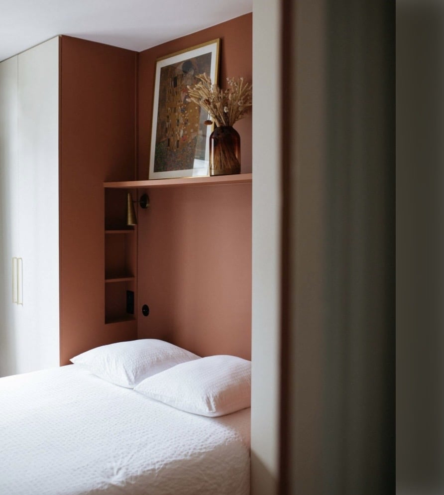 Terracotta built-in wardrobe and shelving in a compact bedroom corner.