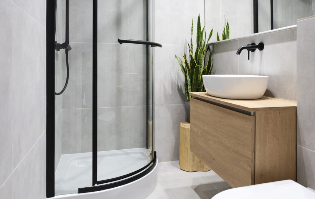 Curved quadrant corner shower with black fixtures and a floating wood vanity with vessel sink