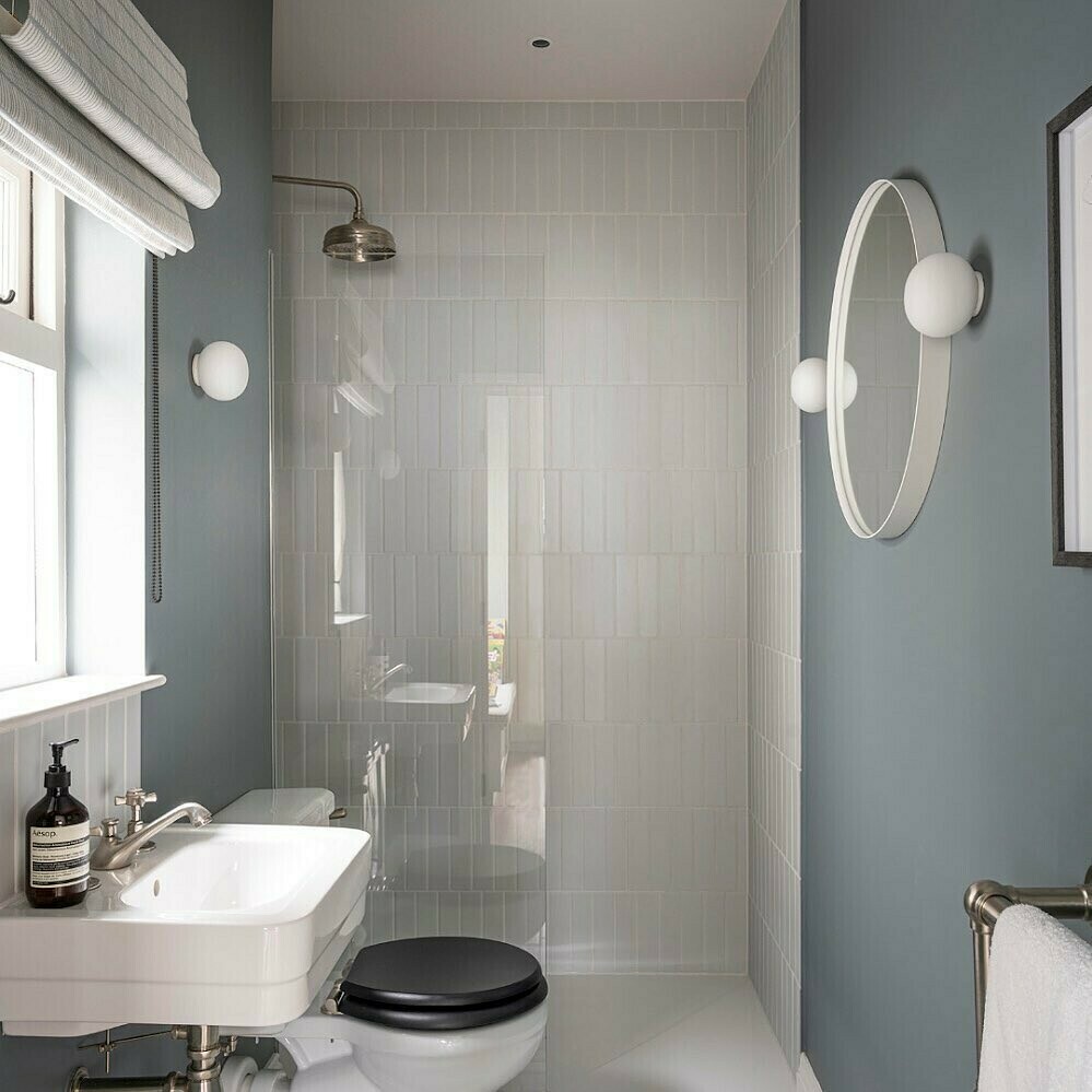 Narrow bathroom with blue-grey walls, glossy metro tile shower and round mirror wall sconce