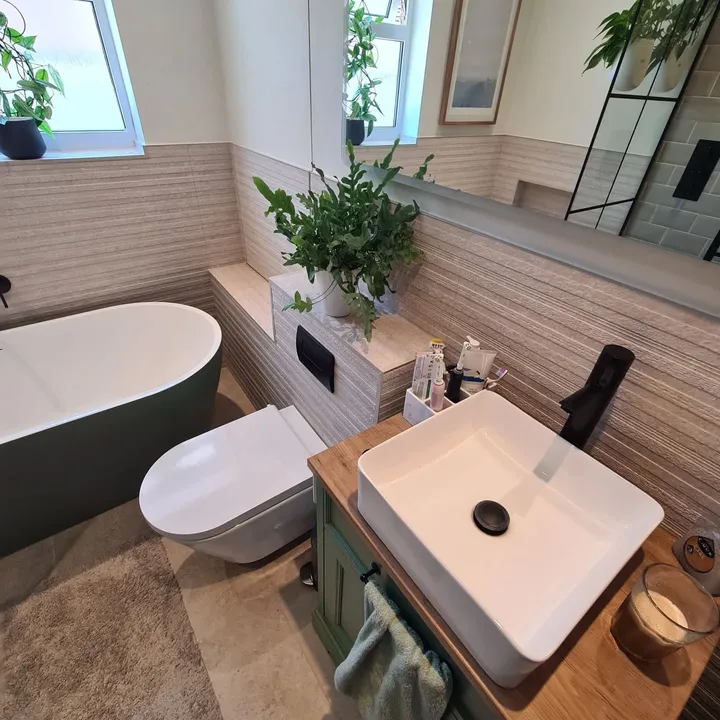 Small galley bathroom with green freestanding bath, wall-mounted toilet and floating vanity with black fixtures