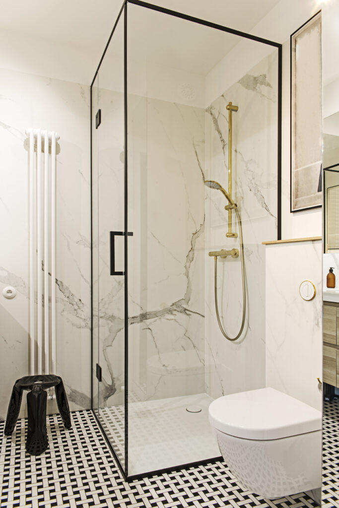 Frameless glass shower enclosure with white marble-effect walls, gold fittings and black-and-white mosaic floor