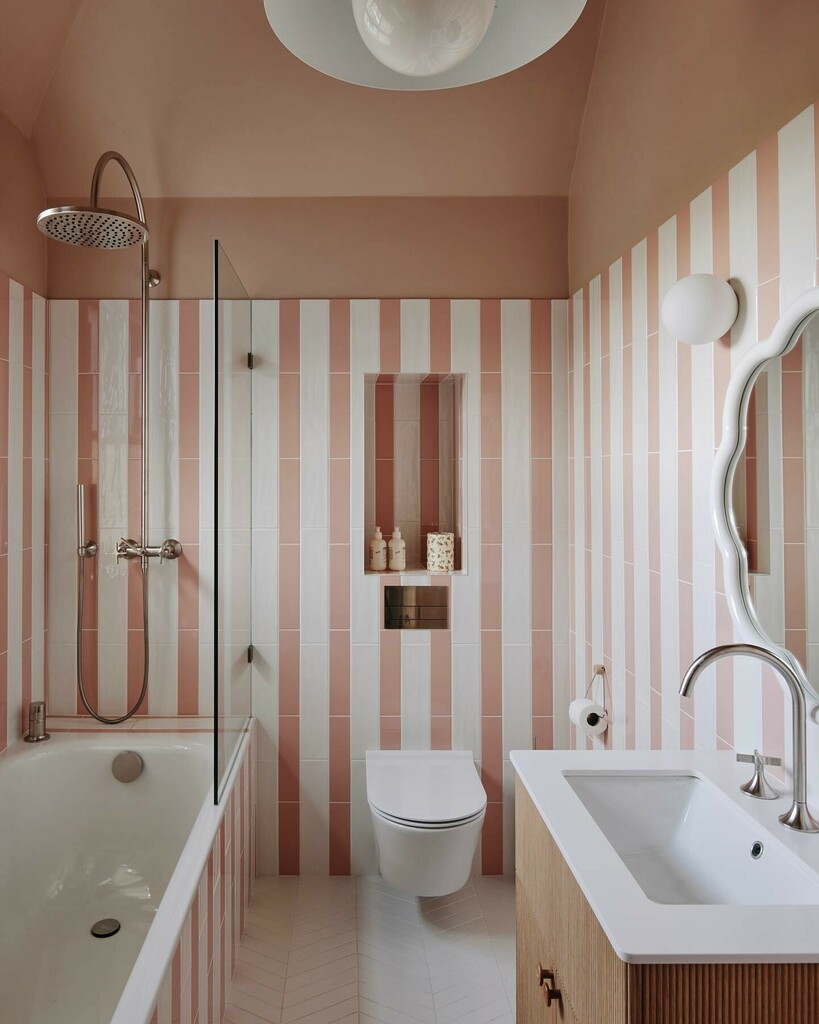 Vertical pink and white striped bathroom tiles with Farrow & Ball Setting Plaster ceiling, wall-mounted toilet and glass shower screen