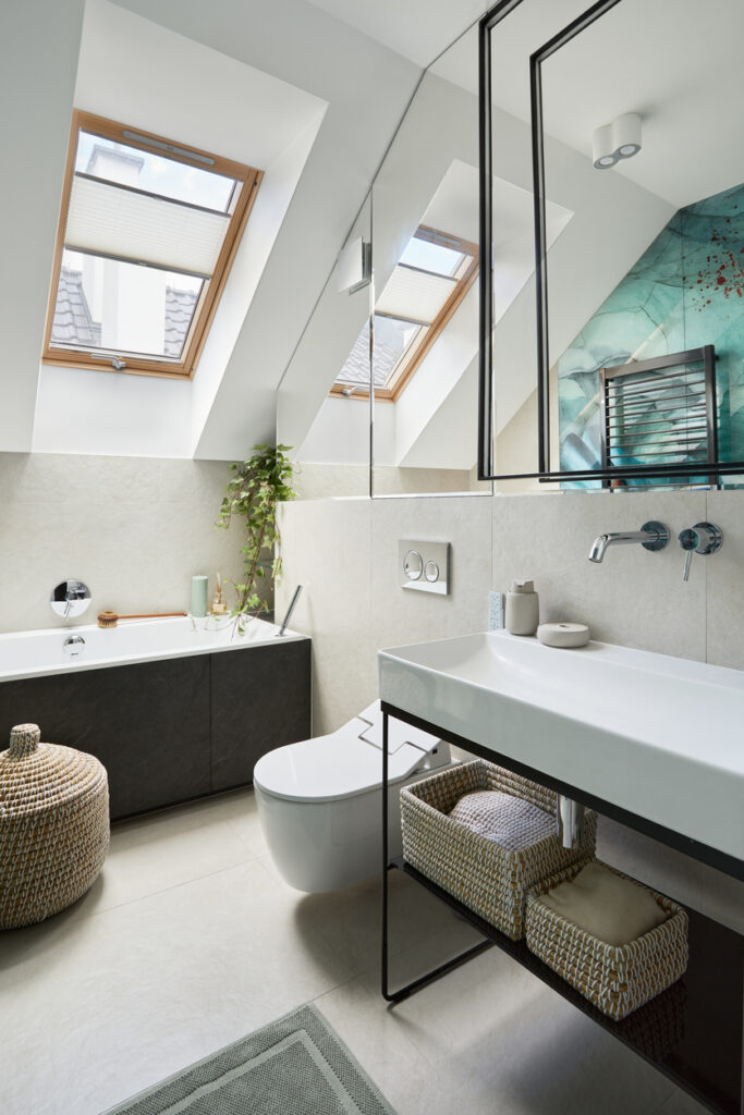 Small eaves bathroom with sloped ceiling, Velux skylights, dark bath panel, wall-mounted toilet and floating basin with woven baskets