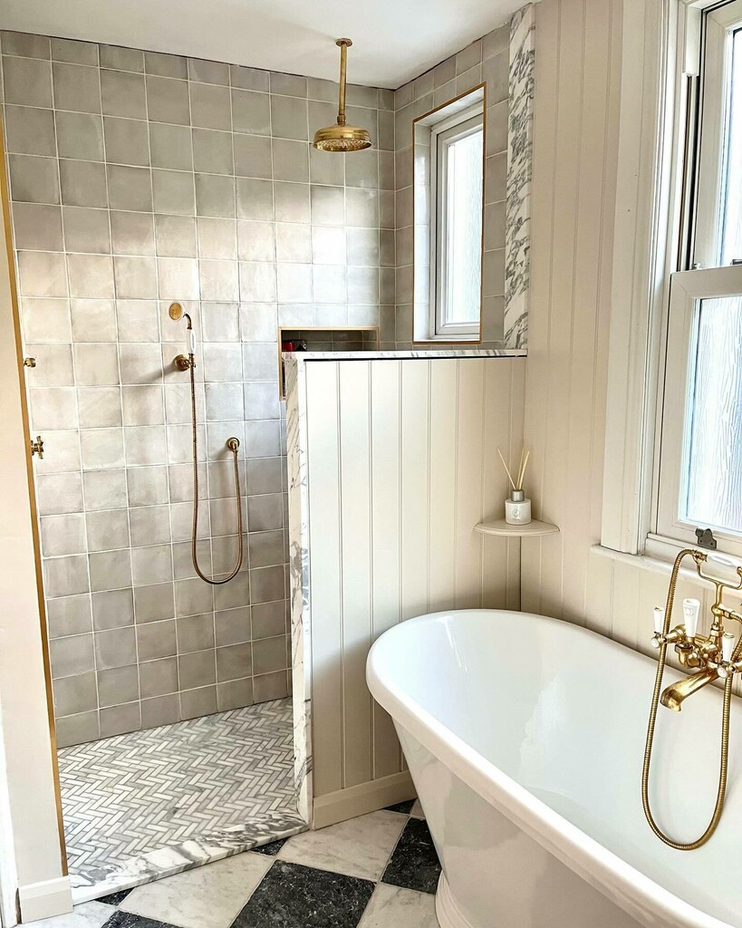 Walk-in shower with zellige-style tiles and herringbone marble floor beside a freestanding bath with brass fittings and checkerboard marble flooring in very small bathroom
