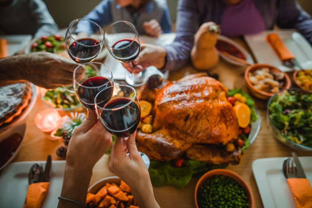 Glass of red wine beside a bottle on a festive table set for Christmas dinner