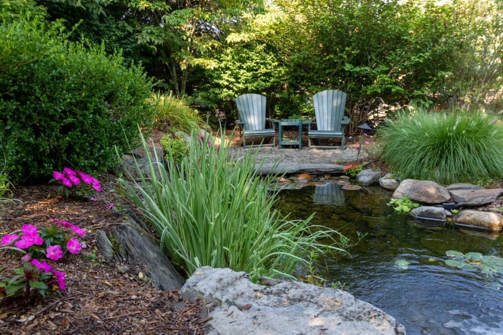 natural garden pond with soft planting and two chairs in a peaceful garden