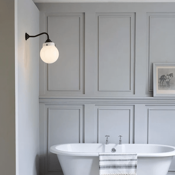 Bronze swan arm wall light with globe shade above a freestanding bath against grey panelled walls