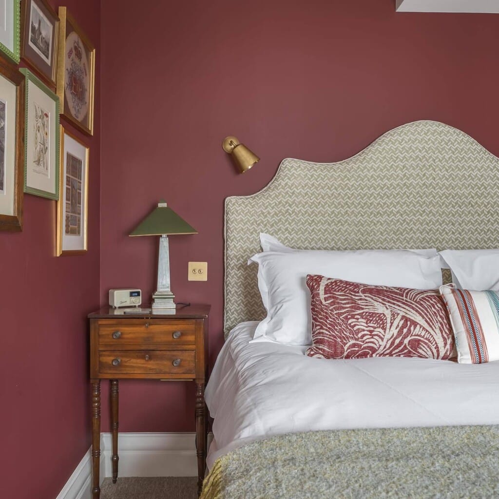 burgundy bedroom with Farrow and Ball Eating Room Red walls, upholstered headboard, gallery wall and antique bedside table