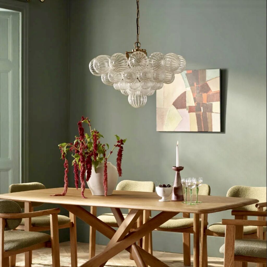 Glass chandelier above a wooden dining table in a moody green dining room