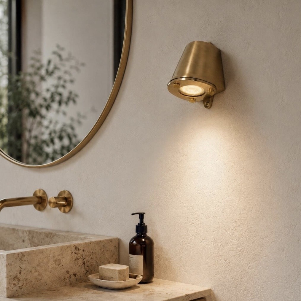 Adjustable raw brass spotlight wall light above a stone bathroom sink