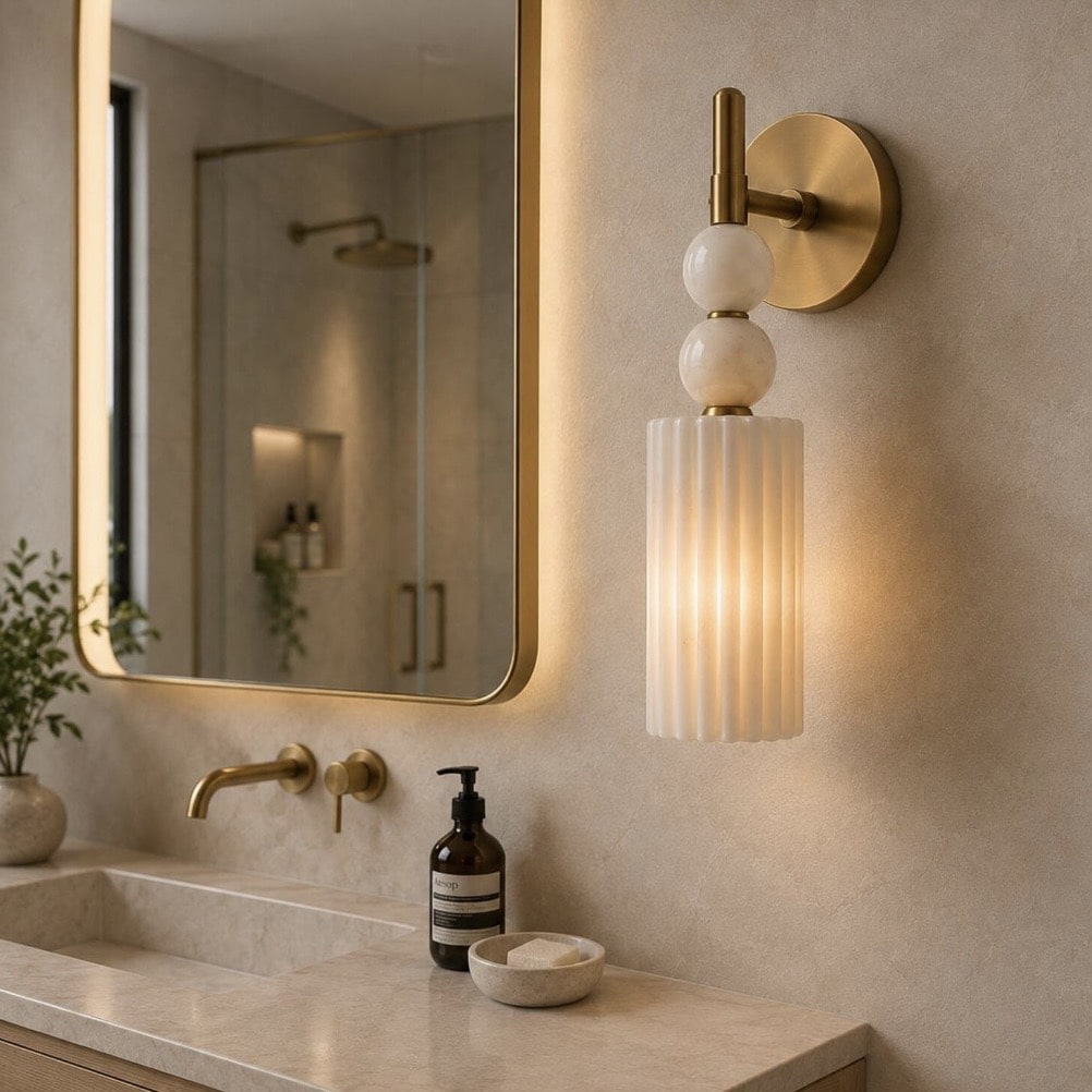 Fluted alabaster wall sconce on a brass fitting beside a gold-framed bathroom mirror