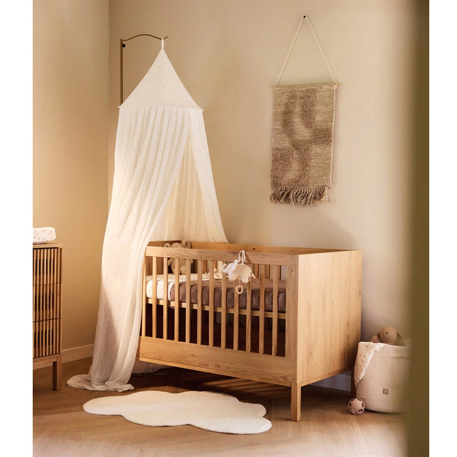 Neutral nursery decor with wooden cot and vintage leaf canopy