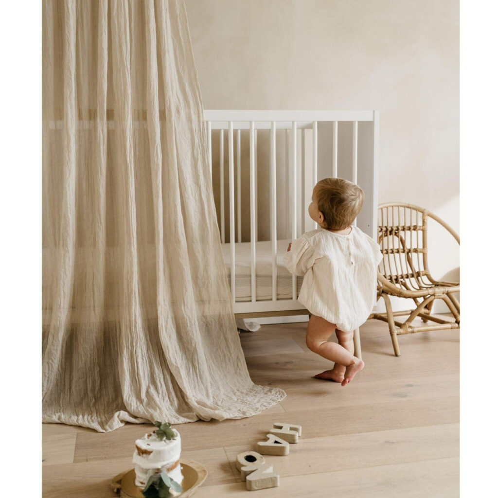 Quax Flow white cot styled with linen curtain and rattan chair