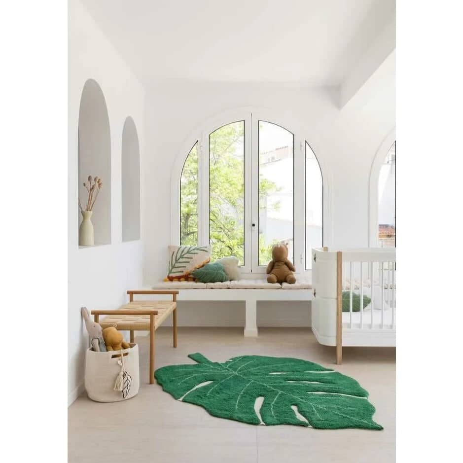 Jungle nursery decor with monstera leaf rug and white cot