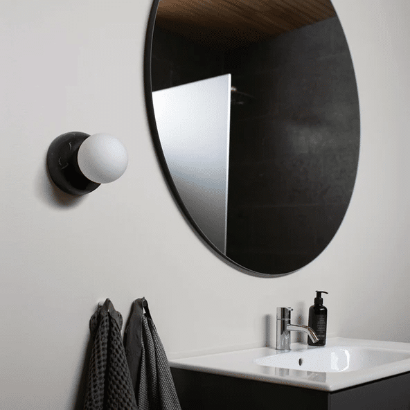 Brown marble-effect wall light beside a black round mirror in a dark-tiled bathroom