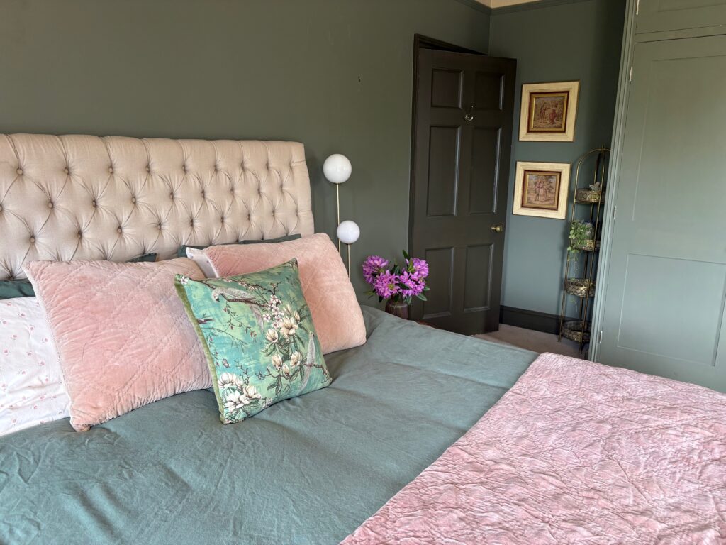 Sage and pink bedroom with sage green walls, blush velvet cushions, a chinoiserie parrot cushion, ditsy floral pillowcases and a painted fitted wardrobe