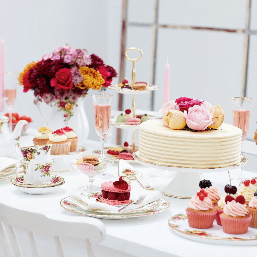 Afternoon tea ideas at home: tiered stand, rose-topped cake, macarons and cupcakes on a white table with Royal Albert Old Country Roses china